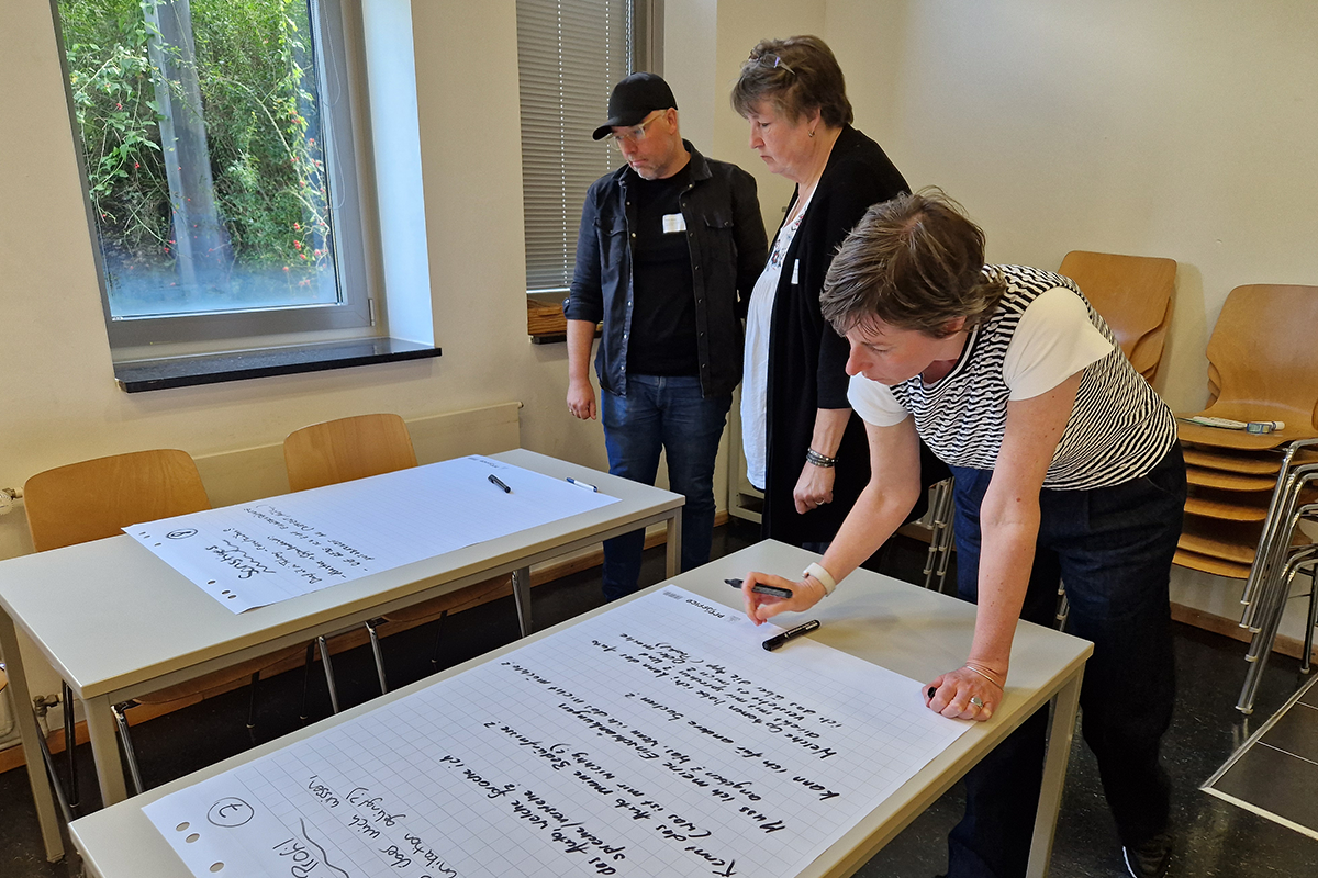 Drei Teilnehmer*innen einer Bürger*innenkonferenz stehen an zwei Tischen und beschriften Flipchart Papier.